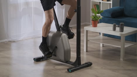 home-training-with-spinning-bike-closeup-view-of-male-legs-on-pedals-sport-and-physical-activity-at-middle-and-old-age
